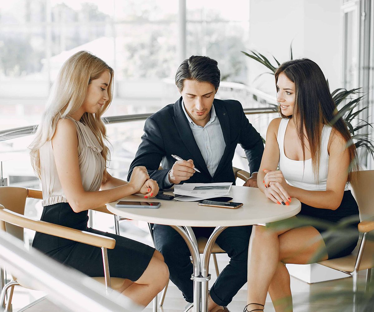 two women and a man sitting at a table | Business Management